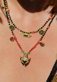 Collier multi-brins avec des perles en pierre verte et des gemmes, accents dorés, et un pendentif avec une émeraude et des pierres colorées, mettant en valeur des designs complexes.