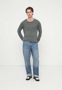 Siva majica z dolgimi rokavi, modre denim kavbojke in črno-bele superge. Priložnostna obleka; majica ima okrogel izrez, kavbojke so rahlo ohlapne.