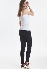 Valge sobiv tank top peenikeste rihmadega, mis on kombineeritud mustade kitsaste pükstega ja mitmevärviliste spordijalatsitega, vaadatuna seljapoolt.