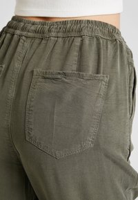 Olivgrön, lätta byxor med elastisk midja och avslappnad passform. Har två bakfickor i lapptäcksstil och en mjuk, slät yta.