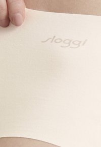 Sloggi naadloze beige stofband, zachte textuur, met subtiele logo-opdruk. Ontworpen voor comfort, met elastische rek.