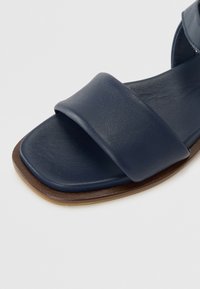 Tummansininen nahkasandaali leveällä yläremmillä, nelikulmaisella varvaskiilalla ja kevyellä puupohjalla. Sileä pinta ja minimalistinen muotoilu.