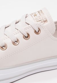 Baskets blanches Converse basse avec lacets blancs, œillets dorés et logo doré "Converse All Star" sur la languette.