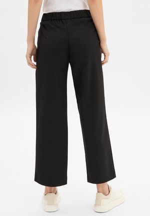 Schwarze weite Hosen mit elastischem Bund, kombiniert mit weißen Sneakers. Der Stoff wirkt weich mit einer glatten Textur und ohne sichtbare Muster.