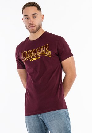 Bordo pamučna majica sa žutim logotipom "LONSDALE" i tekstom "LONDON", okruglim izrezom i kratkim rukavima.