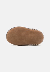 Semelle de chaussure en suède marron texturé avec une forme arrondie. Présente un bord rayé et une surface lisse pour une meilleure adhérence.