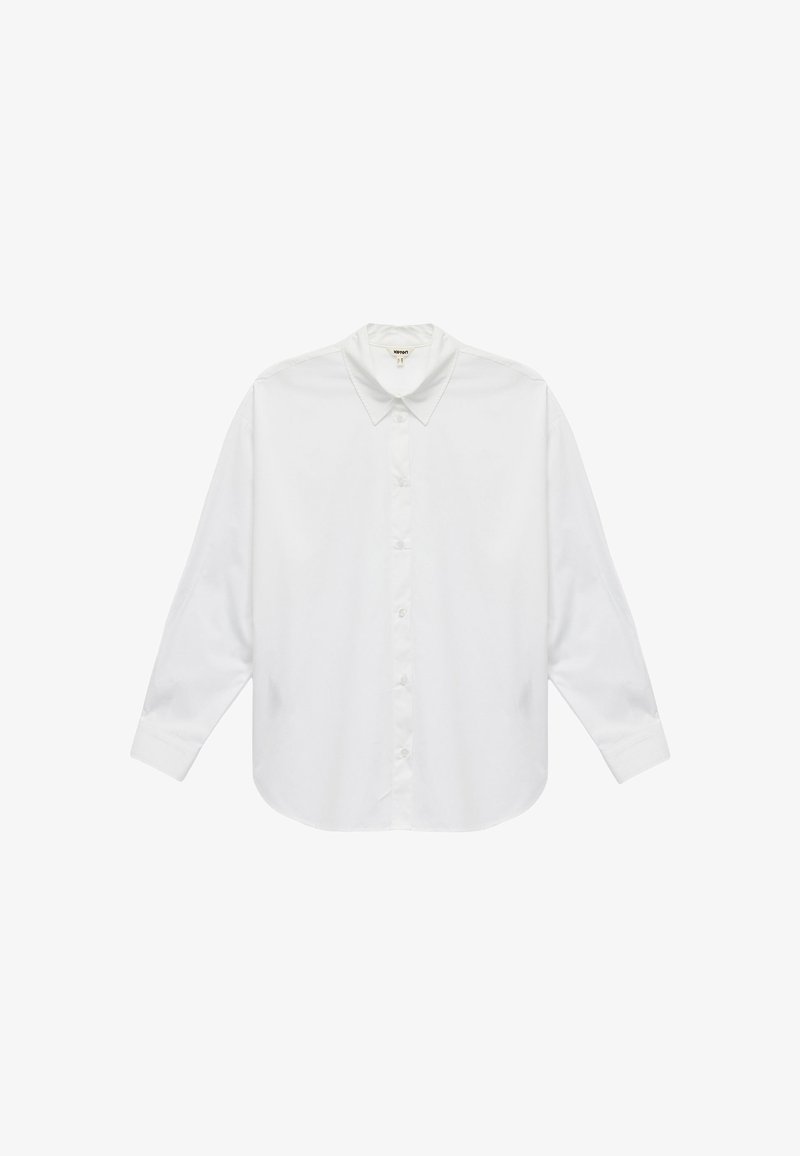 Valkoinen puuvillainen pitkähiha shirt, jossa on klassinen kaulus, napitettava etuosa ja pyöristetty helma. Sileä rakenne, ei kuvioita tai korostuksia.