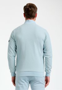 Felpa azzurra chiara con superficie texturizzata, maniche lunghe, polsini a coste e colletto liscio. Accentuata da un piccolo logo sulla manica.