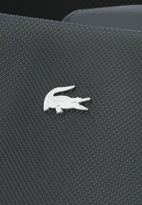 Broche en forme de crocodile argenté sur un fond en tissu noir texturé, présentant des écailles détaillées et un design de bouche ouverte.