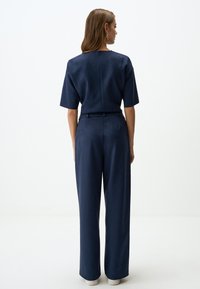 Navyblauwe jumpsuit met korte mouwen, een getailleerde taille en wijde pijpen, gemaakt van een gladde, gestructureerde stof. Ritssluiting aan de achterkant.