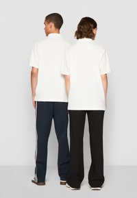 Valged lühikeste varrukatega polo särgid, vaadates selga, koos mereväe ja mustade pükstega. Sile kangas, mugav lõige, minimalistlik disain.