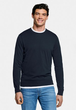 Pull marin en tissu à côtes avec un col rond, superposé à un T-shirt blanc. Associé à un jean en denim bleu clair.