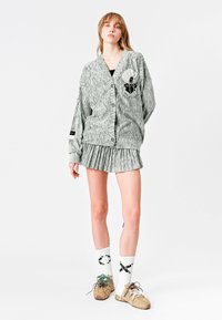 Cardigan a rayas gris y blanco con botones, combinado con una falda plisada. Medias blancas con un patrón negro y zapatillas deportivas beige.