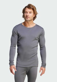 Haut thermique gris à manches longues, ajusté, avec un col rond et une texture lisse. Présente des coutures plates et un contour subtil pour une belle forme.