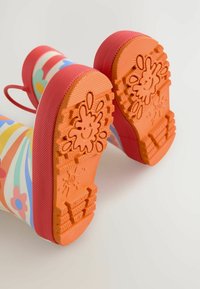 Bunte Gummiregenstiefel mit Blumenmustern, pinken Akzenten und strukturierten orangenen Sohlen in einem verspielten Design.
