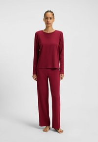 Burgundy lounge set med långärmad topp och vida byxor, tillverkad av mjukt material, med en avslappnad passform och subtil branding.