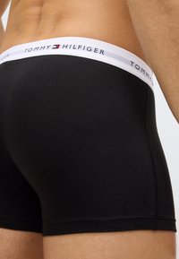 Black cotton boxer briefs with elastic white waistband featuring "TOMMY HILFIGER" logo. Smooth texture and fitted design.