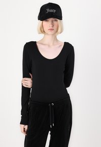 Svart langermet bodysuit med scoop-neck, kombinert med svarte velour joggebukser som har snor. Svart caps med rhinestones "Juicy" logo.