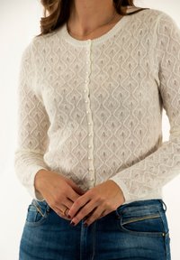 Cardigan bianco lavorato a maglia con motivo a rombi, dotato di scollo rotondo e bottoni perle lungo la parte anteriore. Texture morbida. Maniche lunghe.