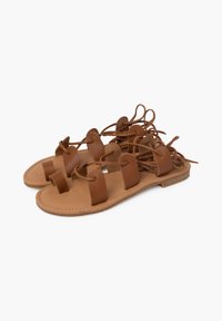 Sandali in pelle marrone con più cinghie e lacci. Suola piatta, texture liscia, design aperto, adatti per essere indossati in climi caldi.