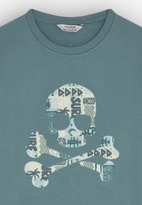 T-shirt in cotone teal con una grande grafica di teschio e ossa incrociate riempita con vari motivi blu. Collo tondo e maniche corte.