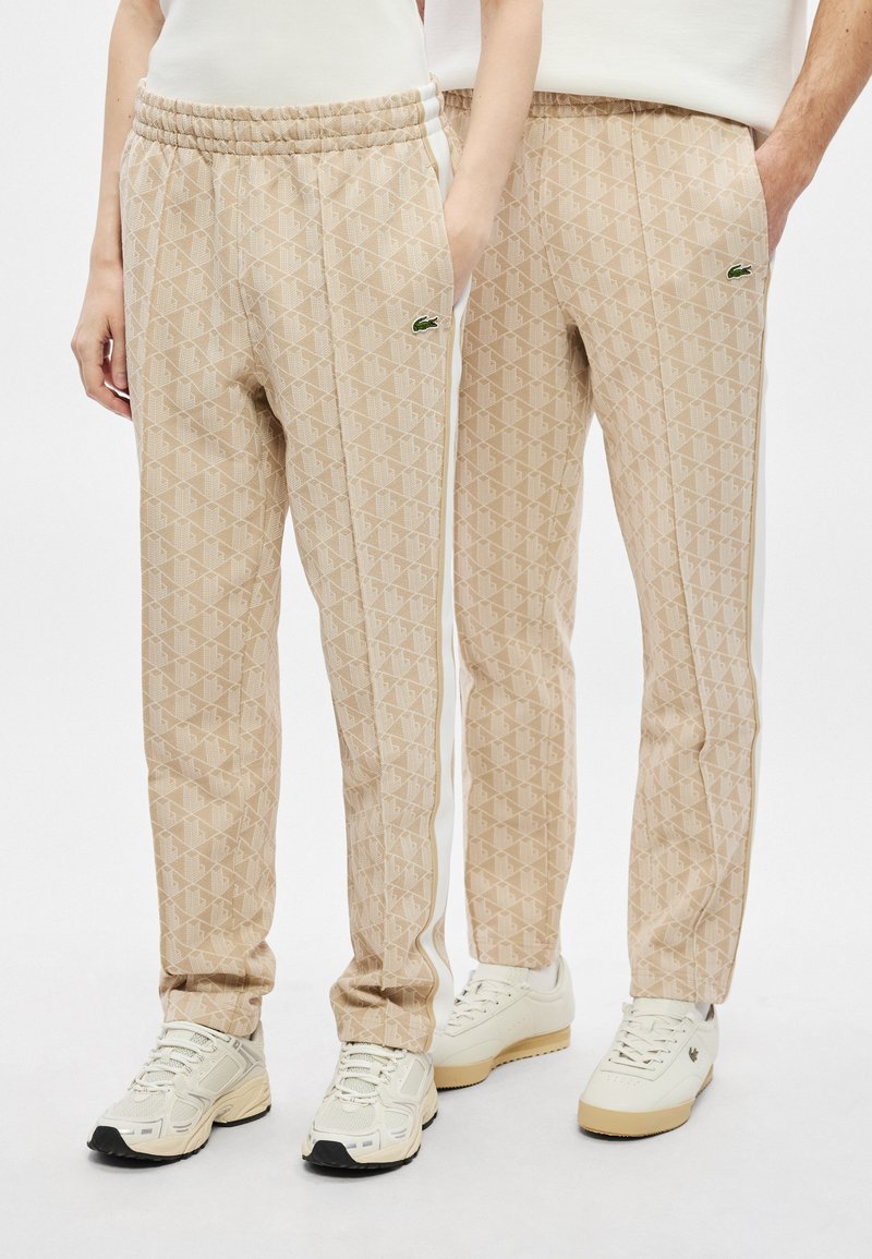 Pantaloni della tuta beige con motivo a trama, vita elasticizzata e tasche laterali, caratterizzati da un design geometrico testurizzato e strisce laterali bianche.