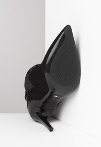 Sort ruskinds højhælet sko med spids tå og glinsende sort sål. Har et elegant design og struktureret hæloverflade. Størrelse 37.