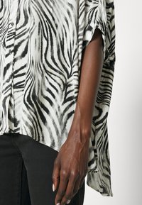 Svartvit randig kortärmad skjorta med knäppning i lätt tyg, med en avslappnad passform och design med hög-låg fåll.