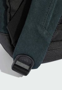 Zaino di colore nero e verde scuro realizzato in un materiale testurizzato con spallacci. Presenta una fibbia in plastica con un logo. La superficie mostra dettagli di cucitura.