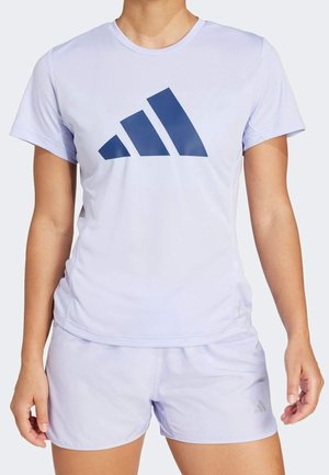 Personne portant un short de sport violet clair et un t-shirt à manches courtes assorti avec un grand logo Adidas bleu foncé sur la poitrine.