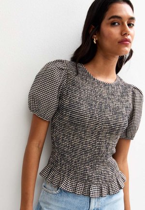 Haut à manches bouffantes en damier noir et crème avec une texture froncée et un ourlet volé, associé à un short en denim bleu clair.