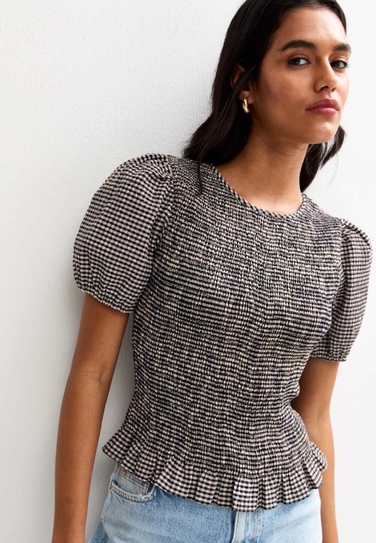 Black and cream checkered puff-sleeve top with gathered texture and a ruffled hem, paired with light blue denim shorts.