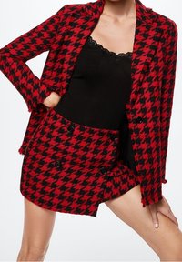 Blazer de pata de gallo rojo y negro con pantalones cortos a juego, con un tejido texturizado, doble botón y bordes deshilachados.