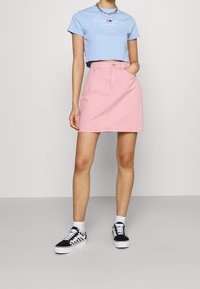 Pink denim skirt with a front pocket and belt loops, paired with a blue cropped T-shirt and black and white checkered sneakers.