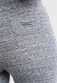 Šedé legíny vyrobené z texturovaného, elastického materiálu s zadní kapsou s logem. Design zahrnuje melírovaný vzhled.