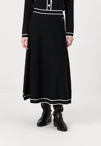 Black knit midi skirt with white accents, featuring a flattering fit, ribbed waistband, and a side slit. Worn with black ankle boots.