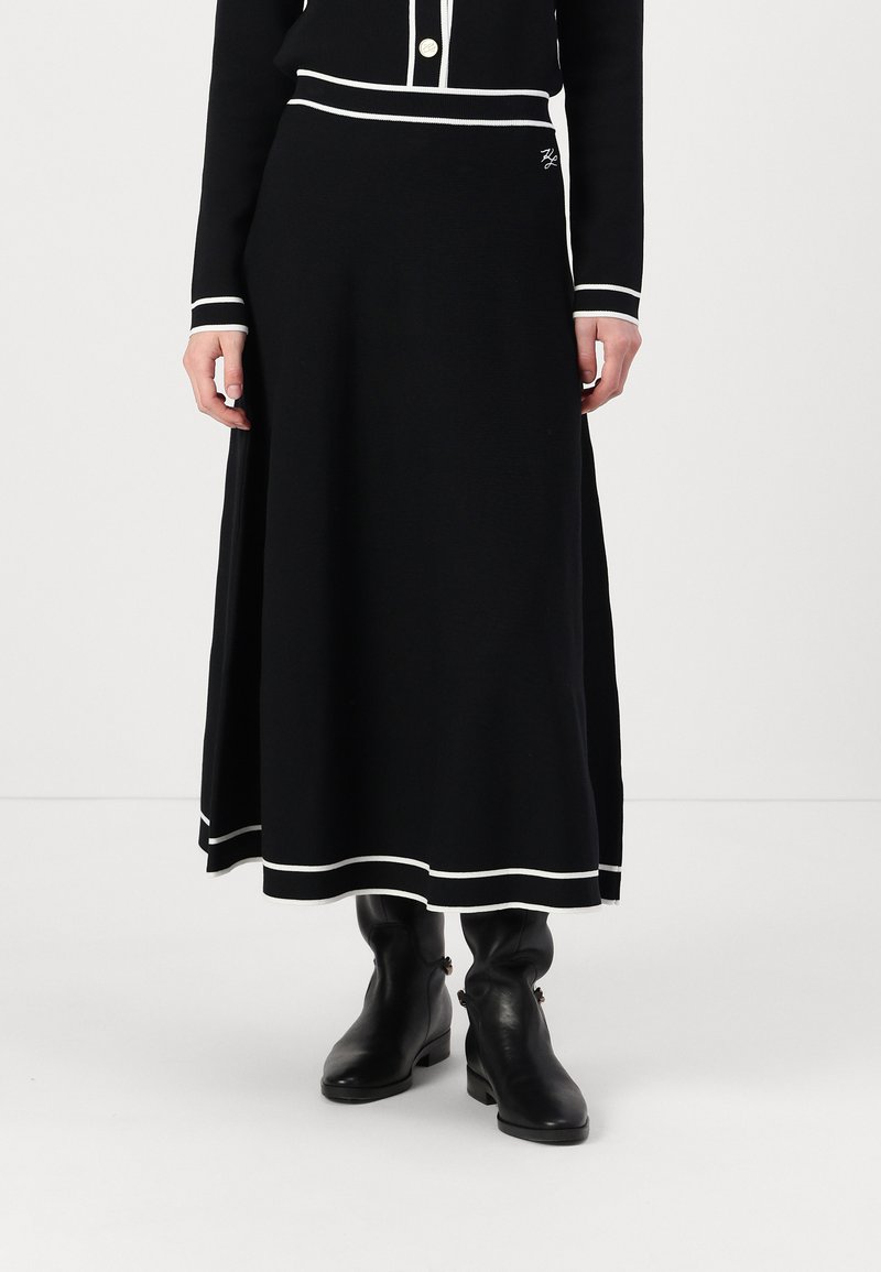 Black knit midi skirt with white accents, featuring a flattering fit, ribbed waistband, and a side slit. Worn with black ankle boots.