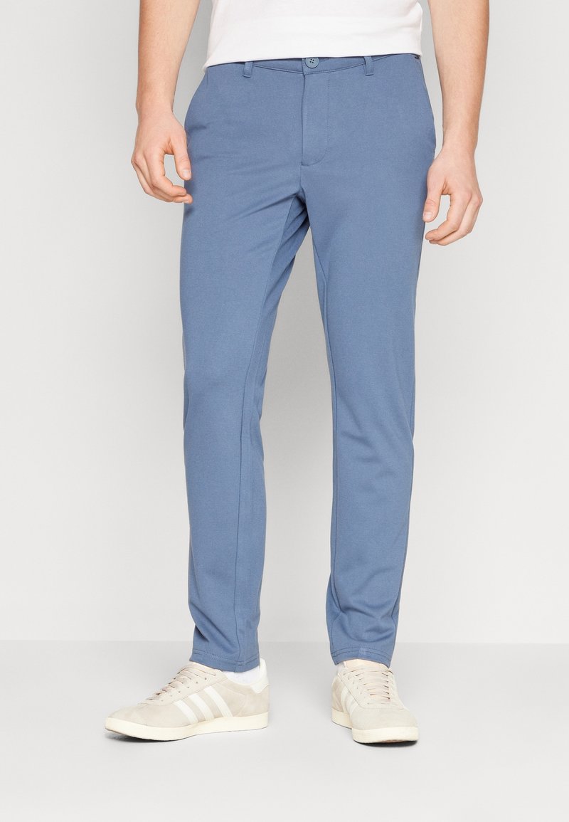 Světle modré slim-fit kalhoty vyrobené z hladkého materiálu, s plochým předním dílem, knoflíkovým zapínáním a bočními kapsami, doplněné o bílé tenisky.