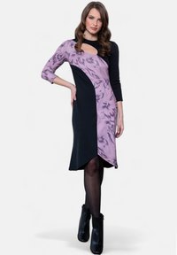 Mekko, jossa on mustaa ja laventelin väriä, pitkät hihat, kukkakuosi yhdellä puolella, epäsymmetrinen helma ja avainaukko kaula-aukossa.