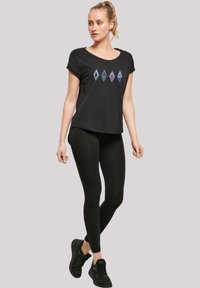 Svart T-skjorte med korte ermer og dyp hals, med fem diamantformede grafiske elementer i blått og lilla. Kombinert med svarte leggings og sko.