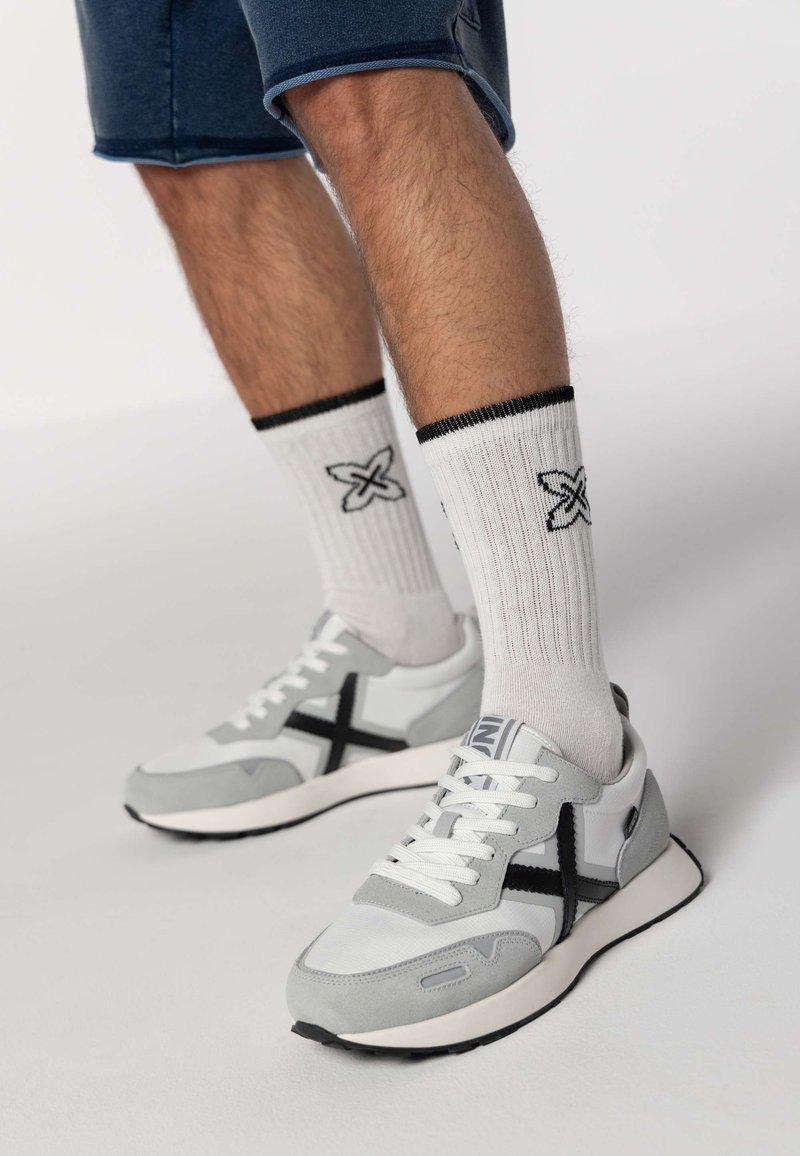 Baskets grises et blanches avec des accents noirs, dotées d'une tige en maille, de suède texturé et de lacets blancs. Portées avec des chaussettes blanches à côtes.