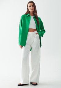 Vihreä napittava paita, valkoinen lyhythihainen toppi, leveät valkoiset housut ja mustat sandaalit. Silkkinen kangas, rento istuvuus ja pitkät hihat.