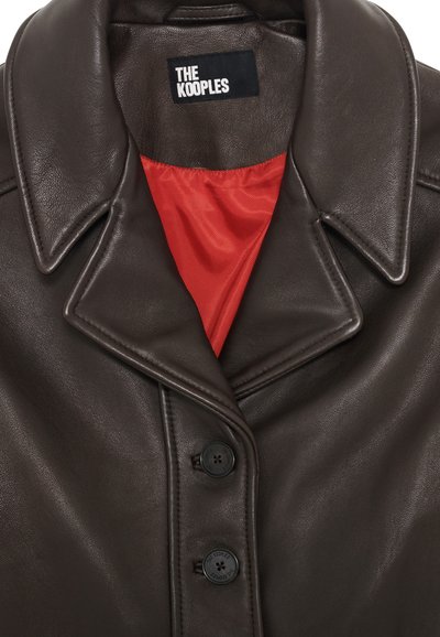 Donkerbruine leren jas met een spitse kraag, twee zwarte knopen en een rode satijnen voering. Etiket met de tekst "THE KOOPLES." Glad materiaal, nauwsluitend ontwerp.