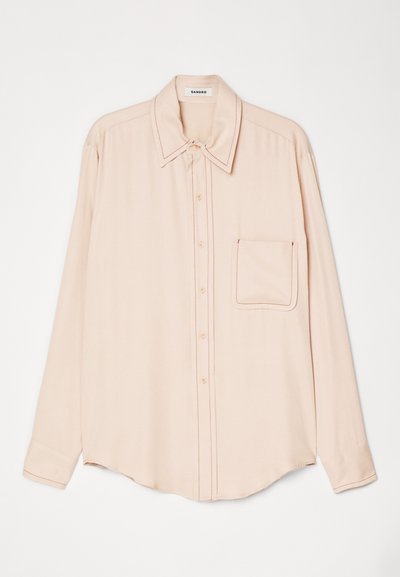 Světle růžová košile s dlouhým rukávem z hladké látky, s špičatým límcem, předními knoflíky a jedním náprsním kapsou s kontrastním švem.