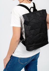 Svart ryggsäck med geometriskt mönster, tillverkad av flexibelt material, med ett handtag på toppen, justerbara remmar och en slät botten.