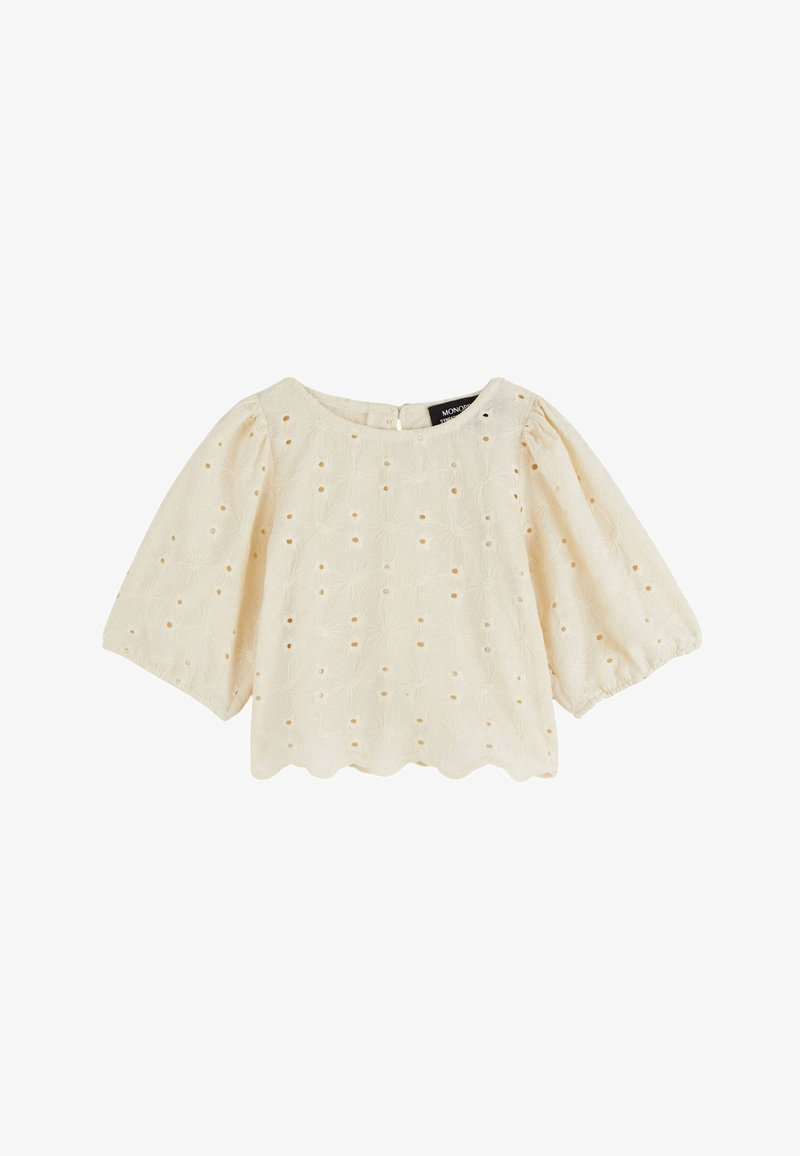 Blouse crème avec des manches courtes bouffantes, motif floral brodé, ourlet festonné et fermeture à bouton au dos.