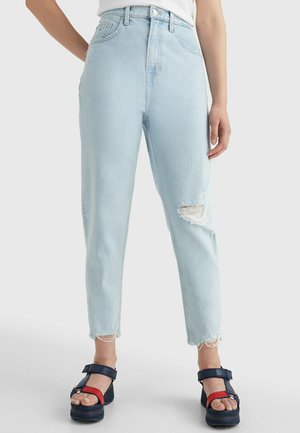 Jeans azzurri a vita alta con dettaglio distrutto sulle ginocchia e orlo sfilacciato, abbinati a sandali platform neri chunky con accenti rossi.