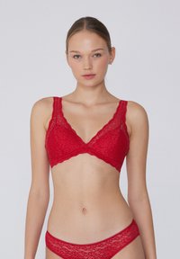 Bralette de encaje rojo con diseño de cuello en V, tirantes anchos y un borde ligeramente ondulado. La textura tiene un patrón intrincado, proporcionando una apariencia delicada.