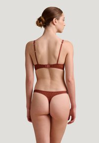 Ensemble de lingerie composé d'un soutien-gorge et d'un string en dentelle bordeaux, mettant en avant des motifs géométriques complexes, avec des bretelles réglables et un fermoir à l'arrière.