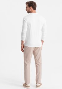 Långärmad, vit skjorta sedd bakifrån, i kombination med ljusbeiga byxor och beige sneakers. Mjukt tyg, figursydd design, inga synliga mönster.